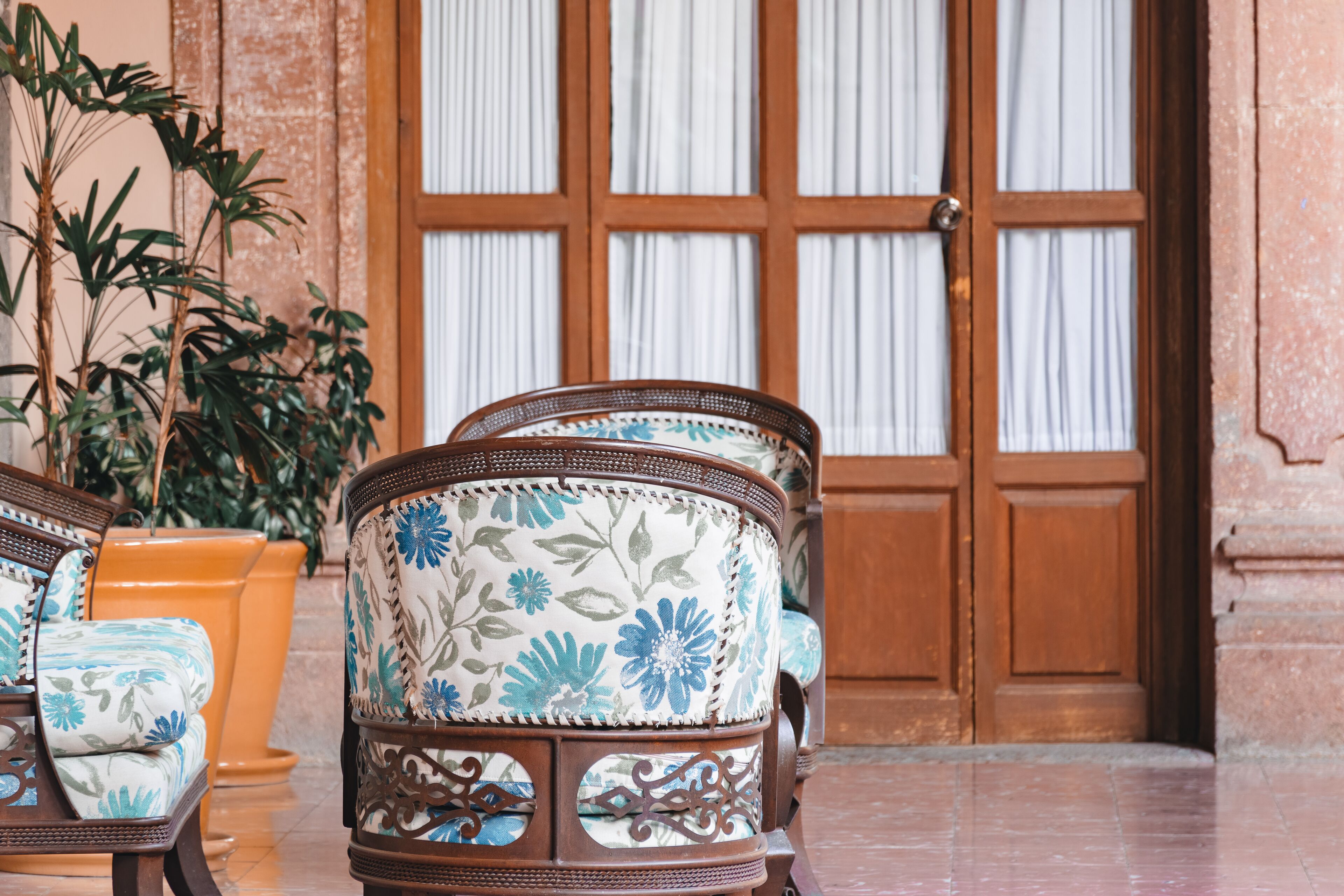 A room with a wooden door, a potted plant, and two upholstered chairs with floral upholstery.