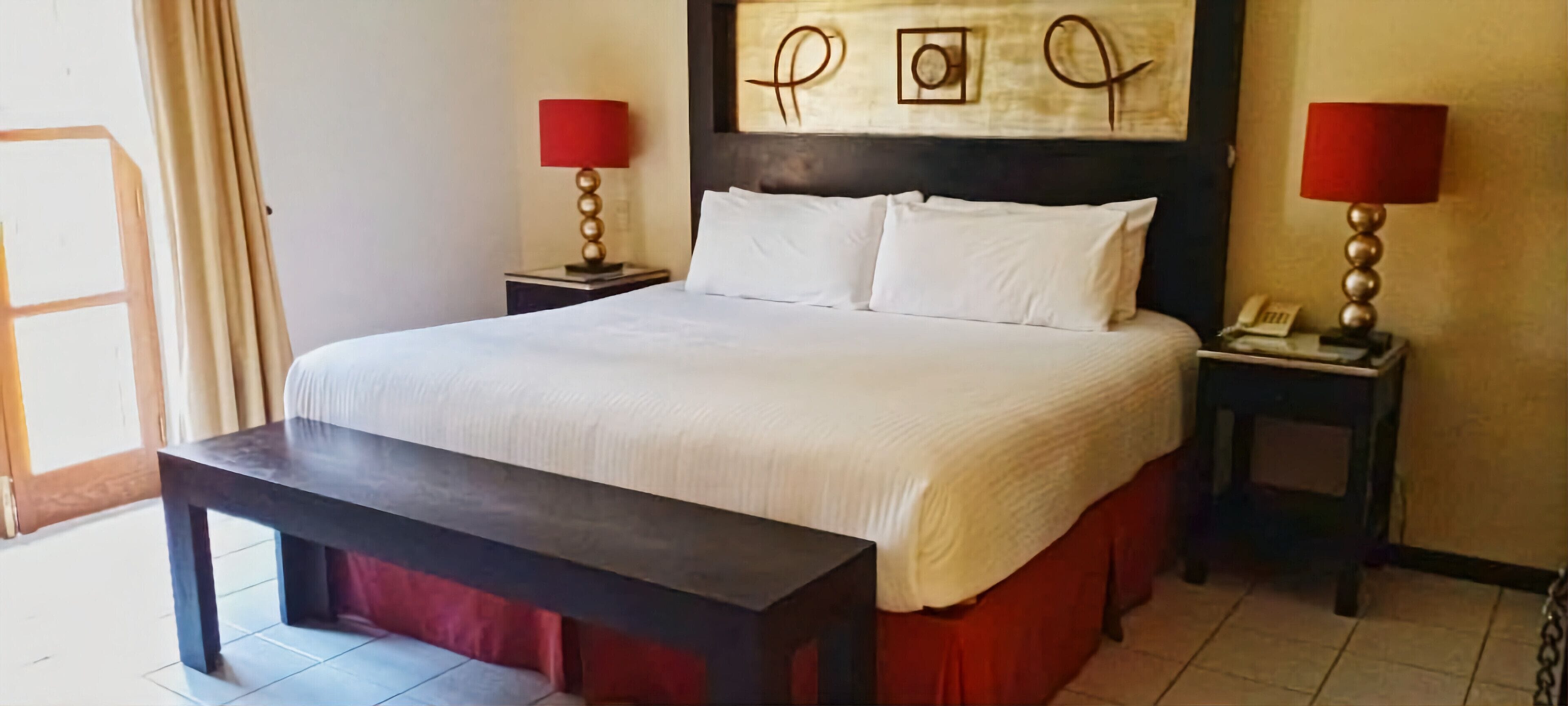 A neatly made bed with white linens, a wooden headboard, and two bedside tables with lamps.