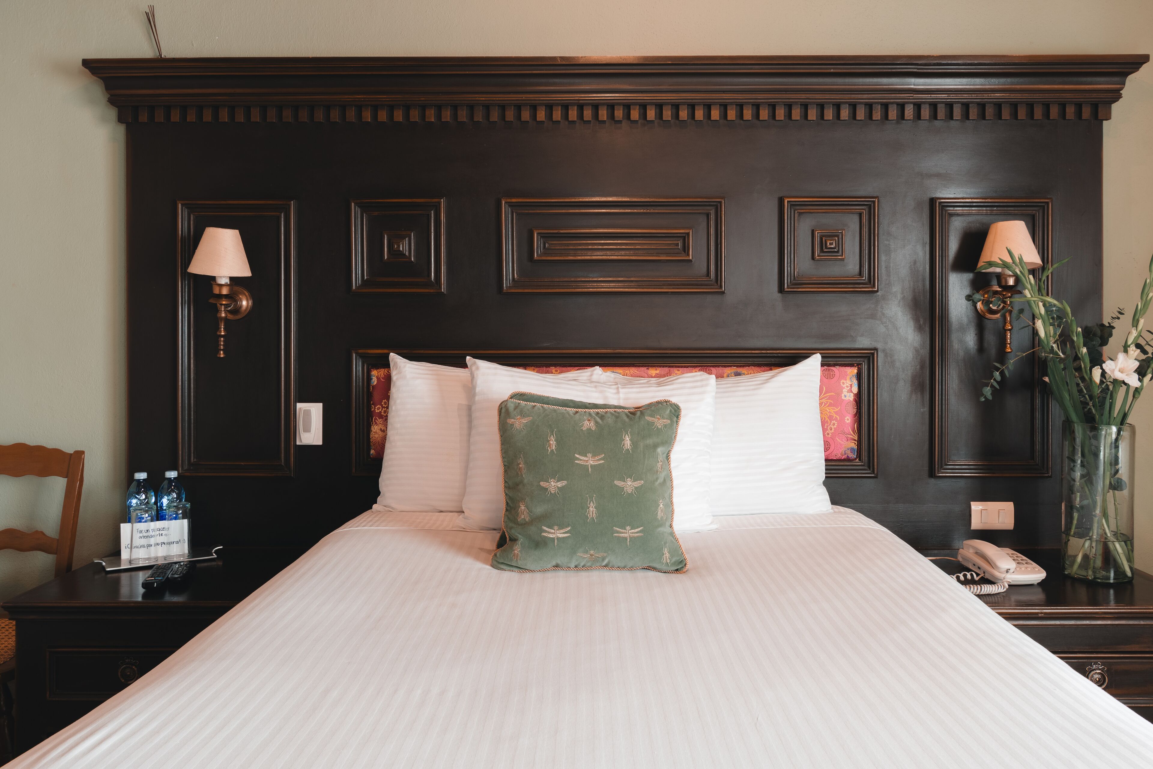 A neatly made bed with a green pillow, a bedside table with a lamp, and a vase with flowers.
