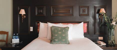 A neatly made bed with a green pillow, a bedside table with a lamp, and a vase with flowers.