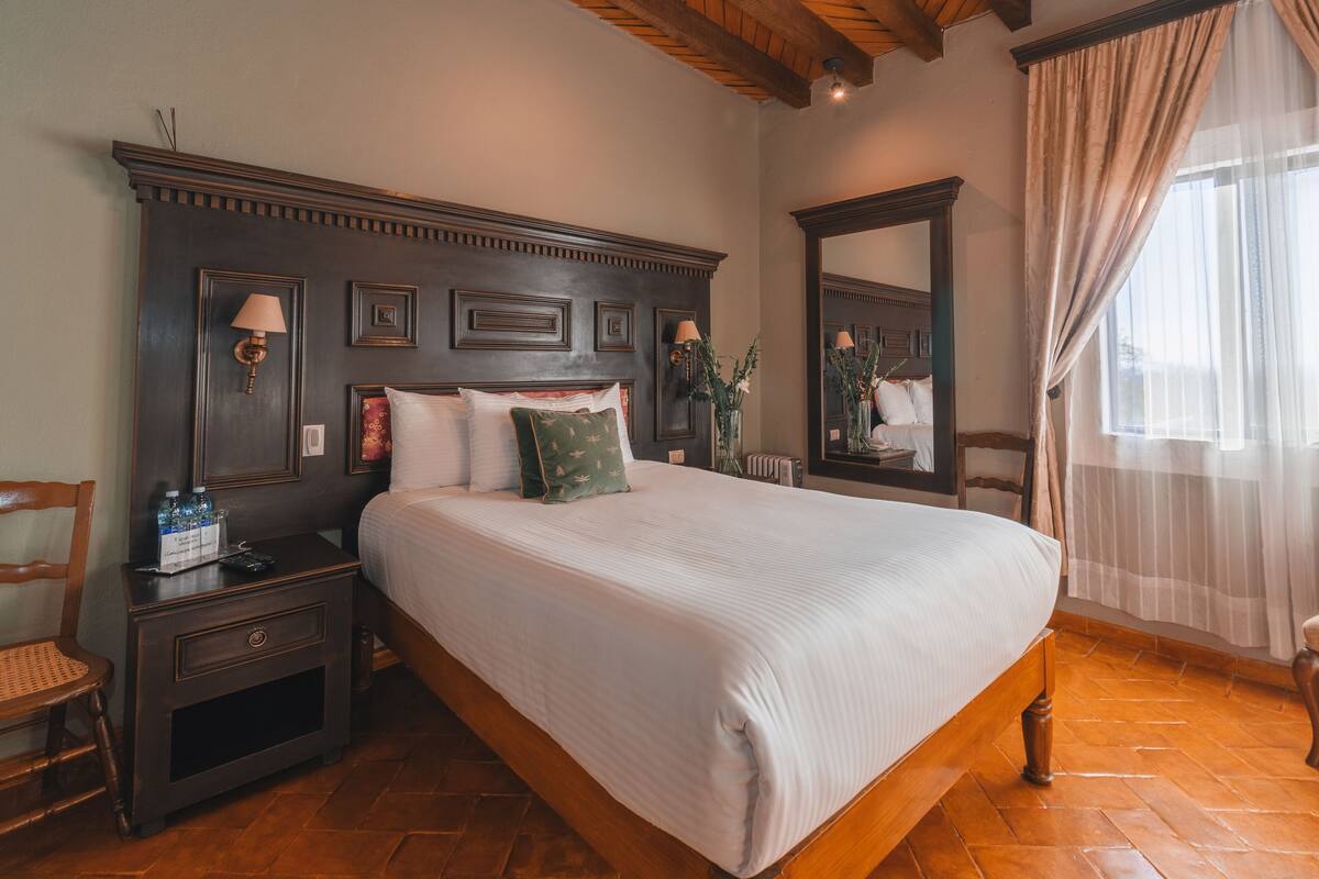 Un dormitorio ordenado con una cama grande, una mesita de noche, un aparador y un espejo.