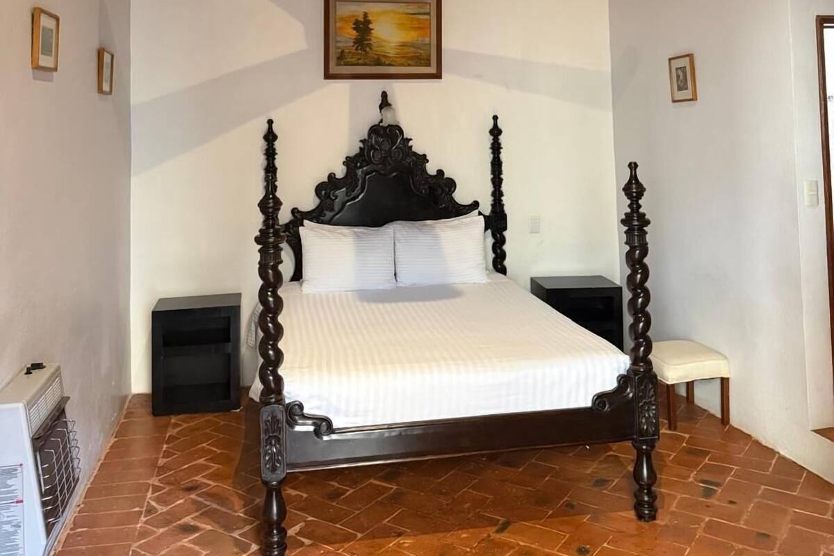 Un dormitorio con cama con dosel, ventilador de techo, equipo de aire acondicionado y un cuadro en la pared.