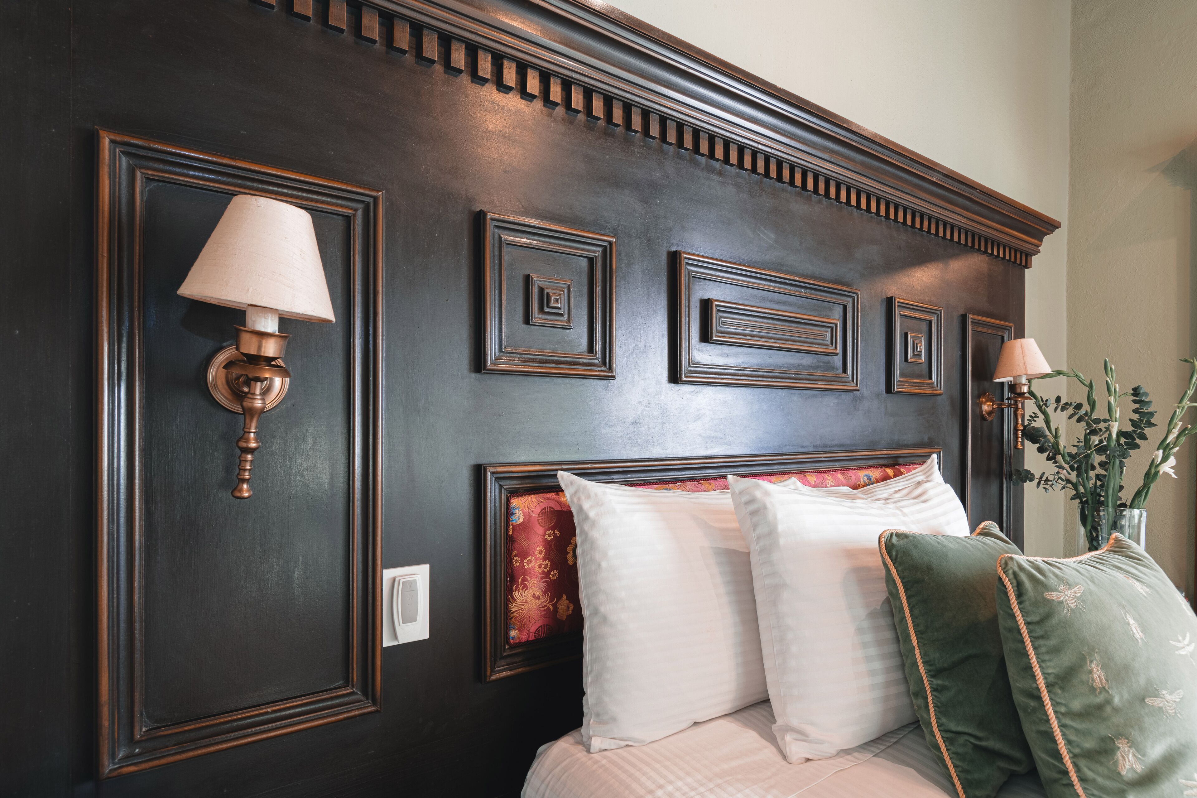 A bedroom with a dark wood headboard, a red and gold headboard panel, and a white bed with green and white pillows.