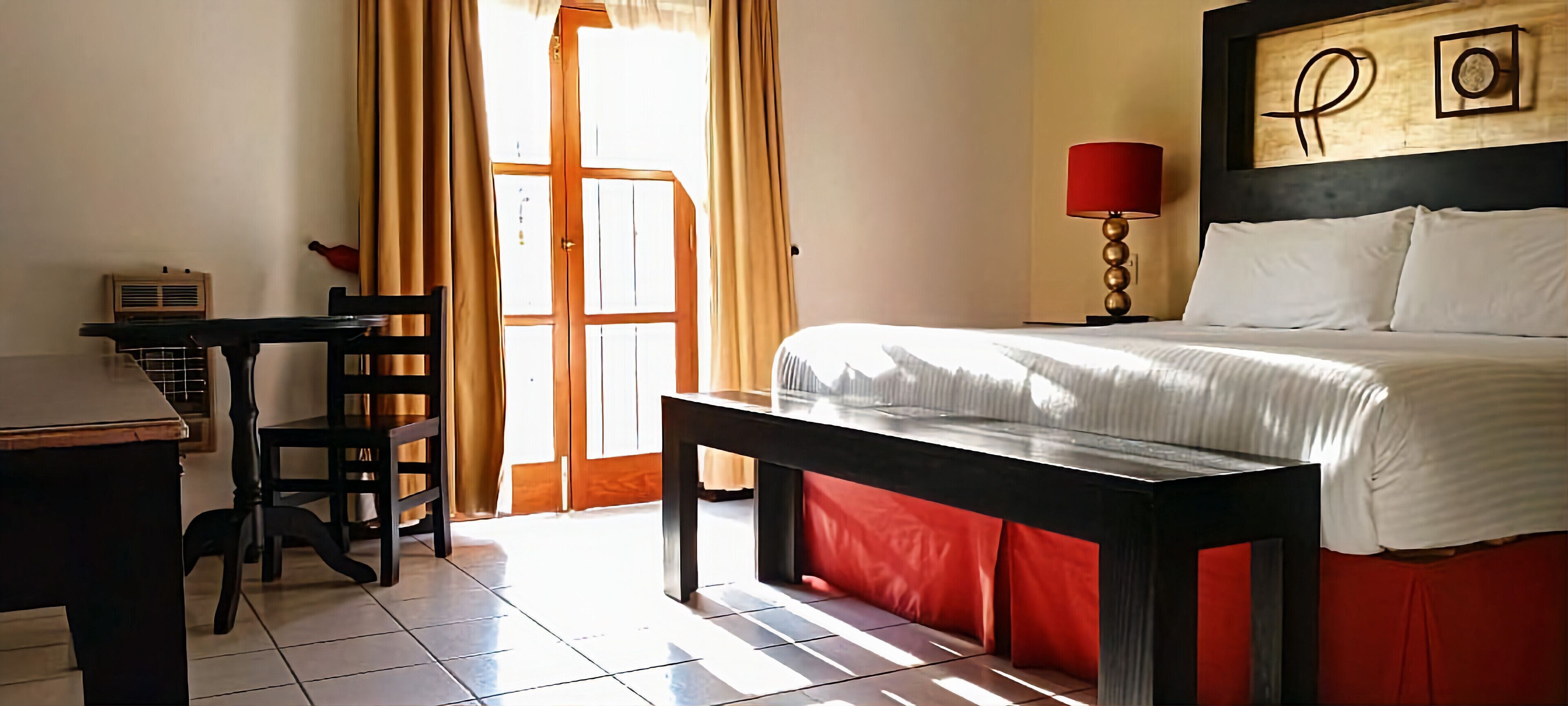A hotel room with a bed, a desk, a chair, a lamp, and a window with curtains.
