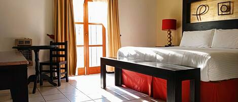 A hotel room with a bed, a desk, a chair, a lamp, and a window with curtains.