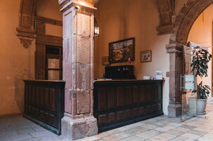 Un vestíbulo con mostrador de recepción, columnas de piedra, un cuadro y una planta en maceta.