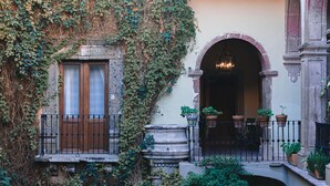 Une façade d’immeuble avec une fenêtre, un balcon orné de plantes en pot et une porte d’entrée en arc de cercle.