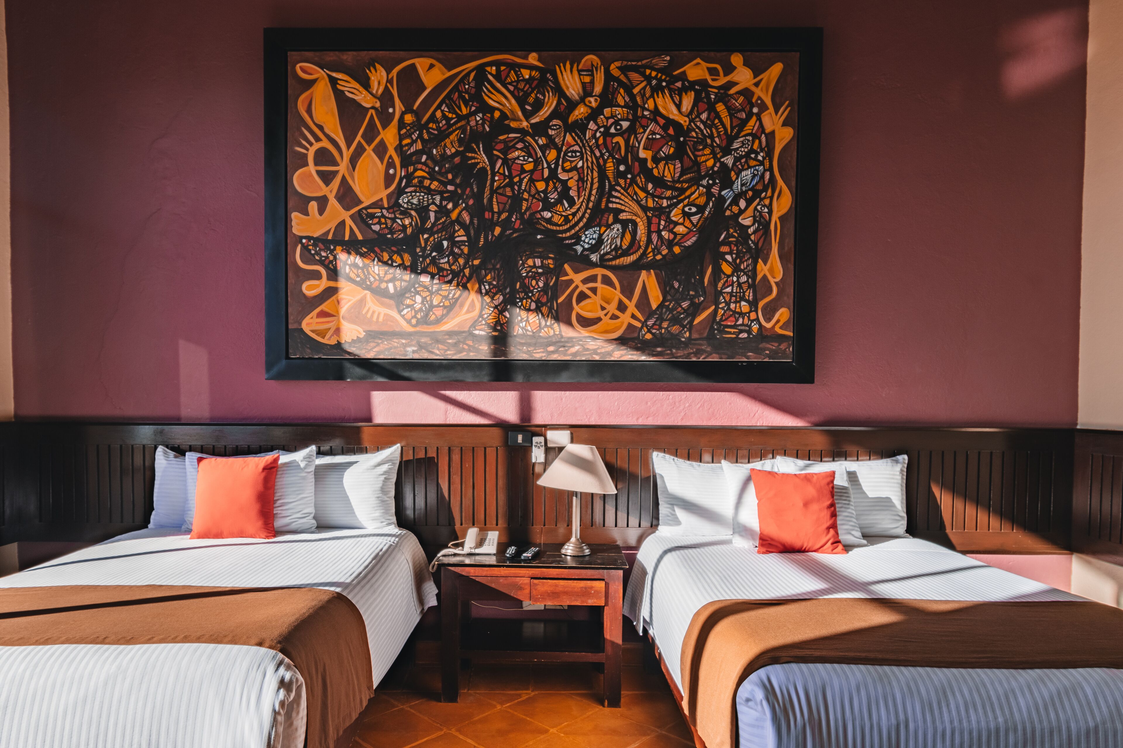 A hotel room with two beds, a nightstand, a lamp, and a large abstract artwork on the wall.