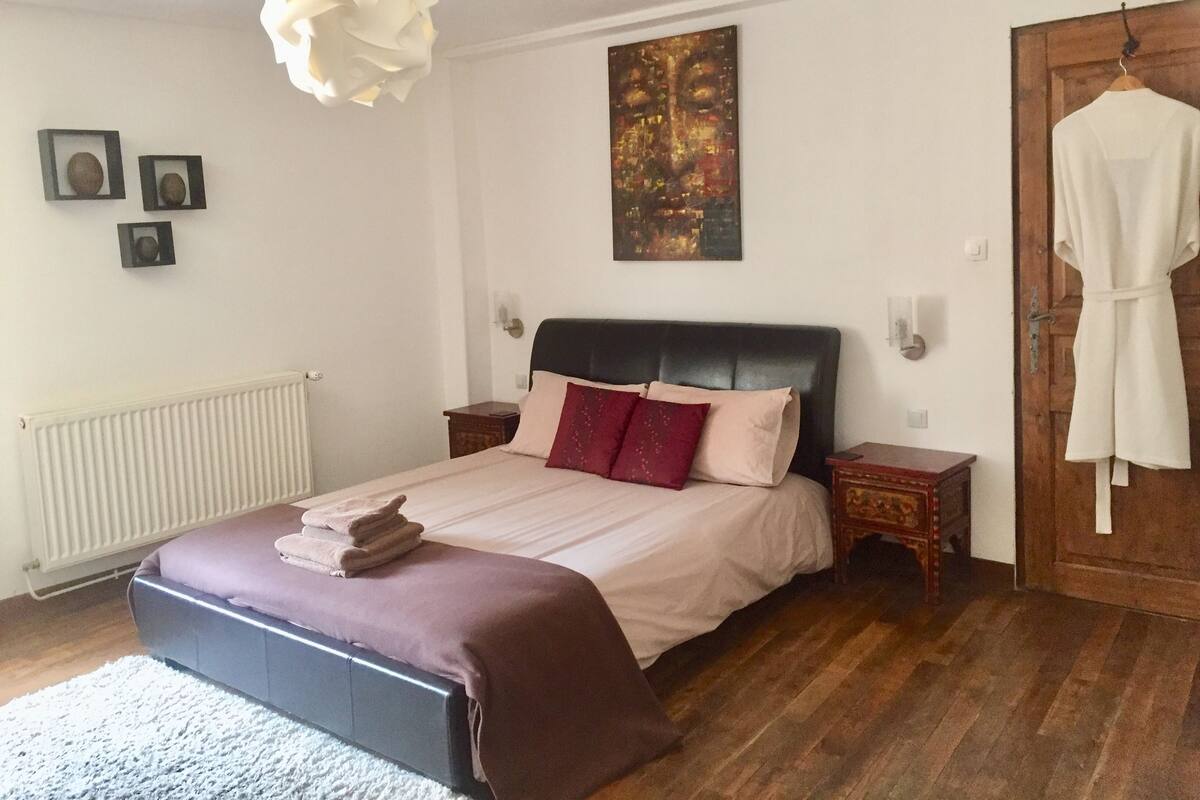 Ein Schlafzimmer mit einem Bett, einem Heizkörper, einem Holzboden, einem weißen Bademantel, der an der Tür hängt, und einem Bild an der Wand.