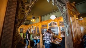 A restaurant with wooden interiors, green booths, and hanging lights.