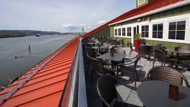 A waterfront restaurant with outdoor seating overlooking a river.