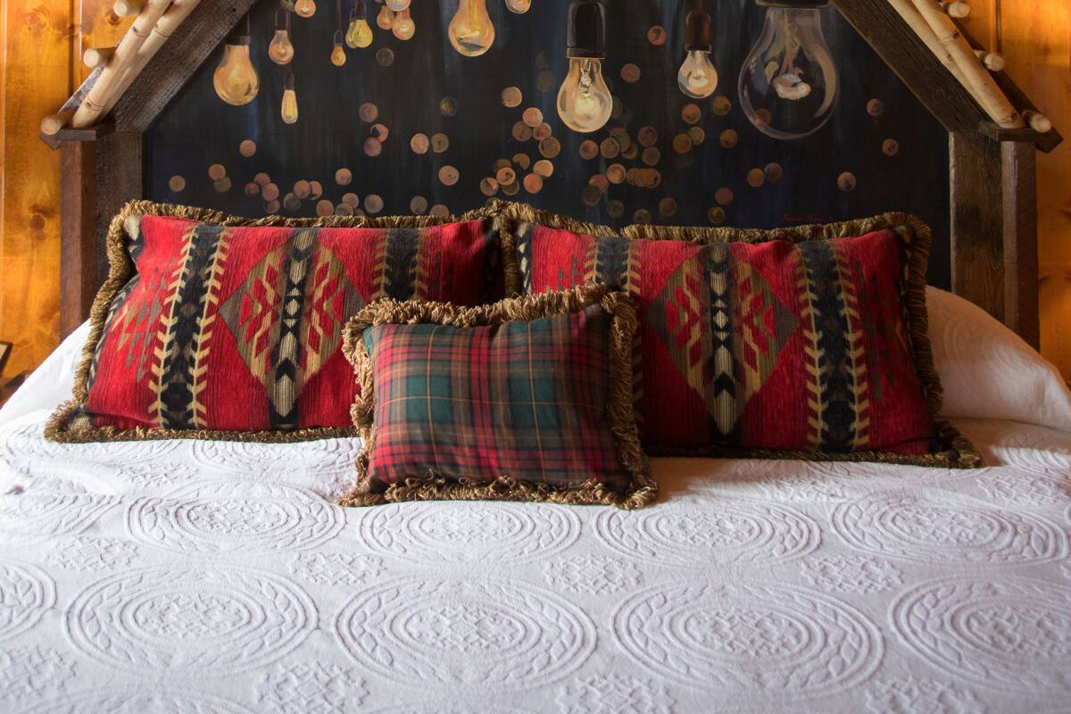 Une chambre avec un plafond en bois, un toit à pente et un lit agrémenté d’oreillers à motifs.