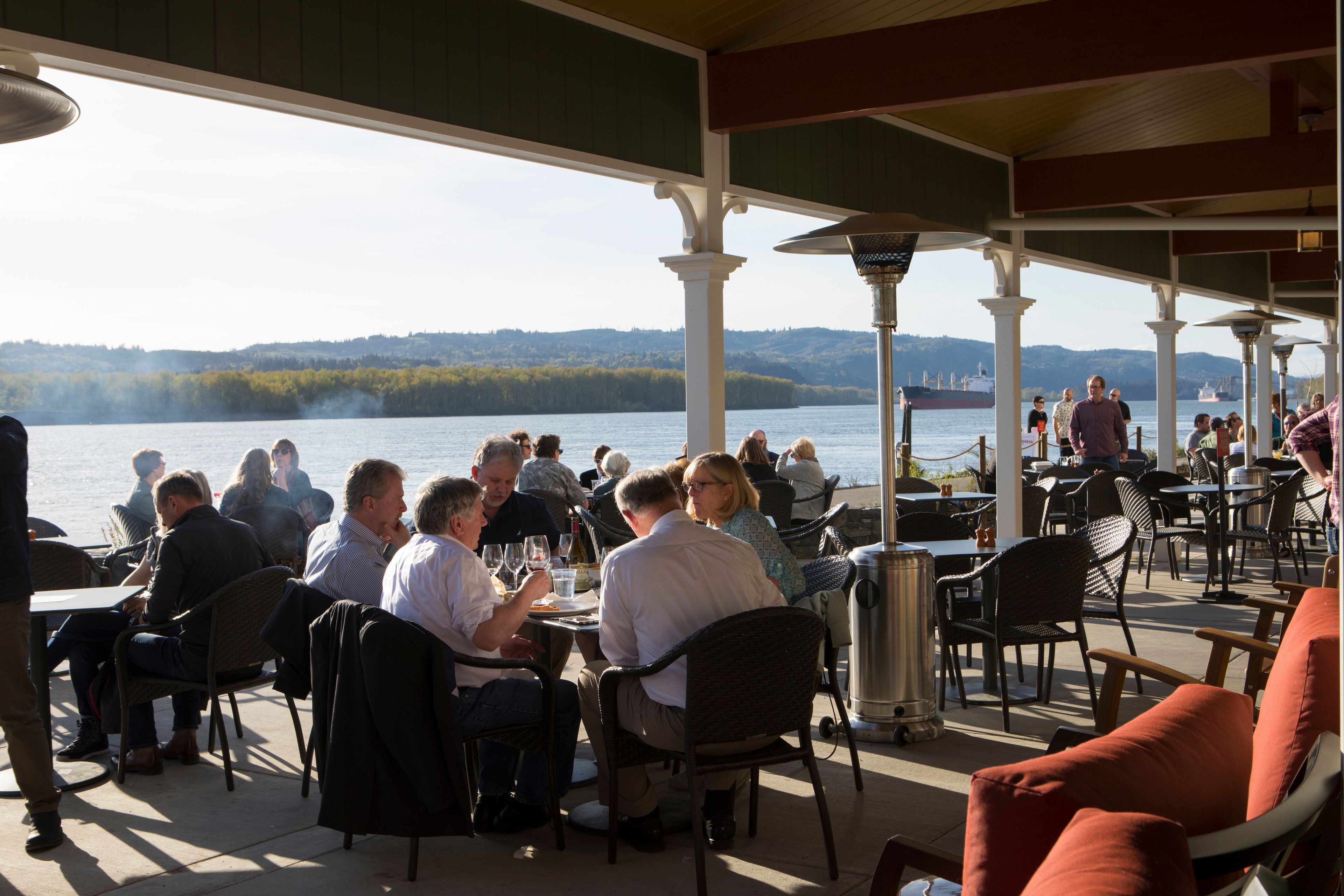 An outdoor dining area with tables and chairs, overlooking a body of water with boats.