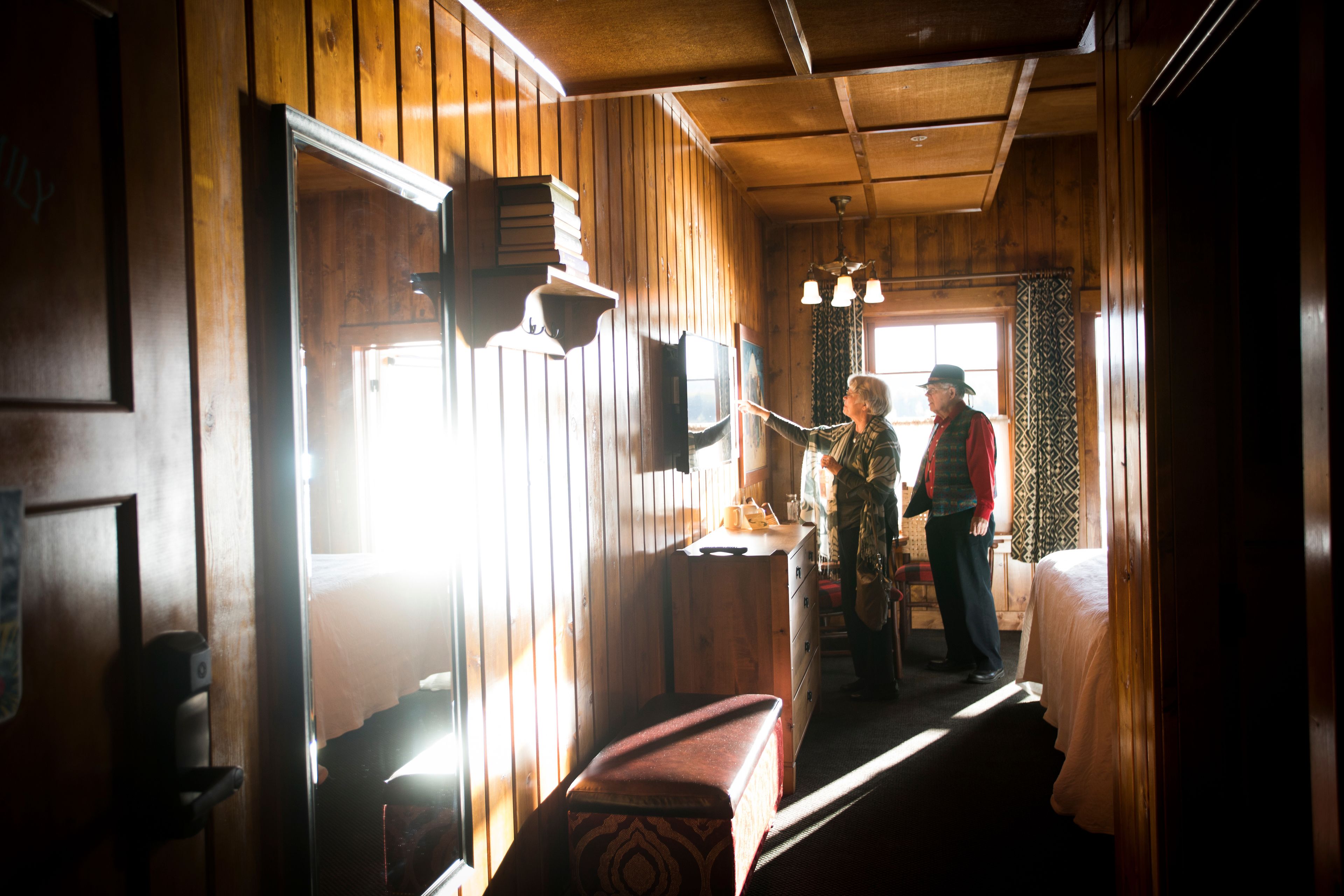A cabin interior with wooden walls, a bench, a small table, and a window with curtains.