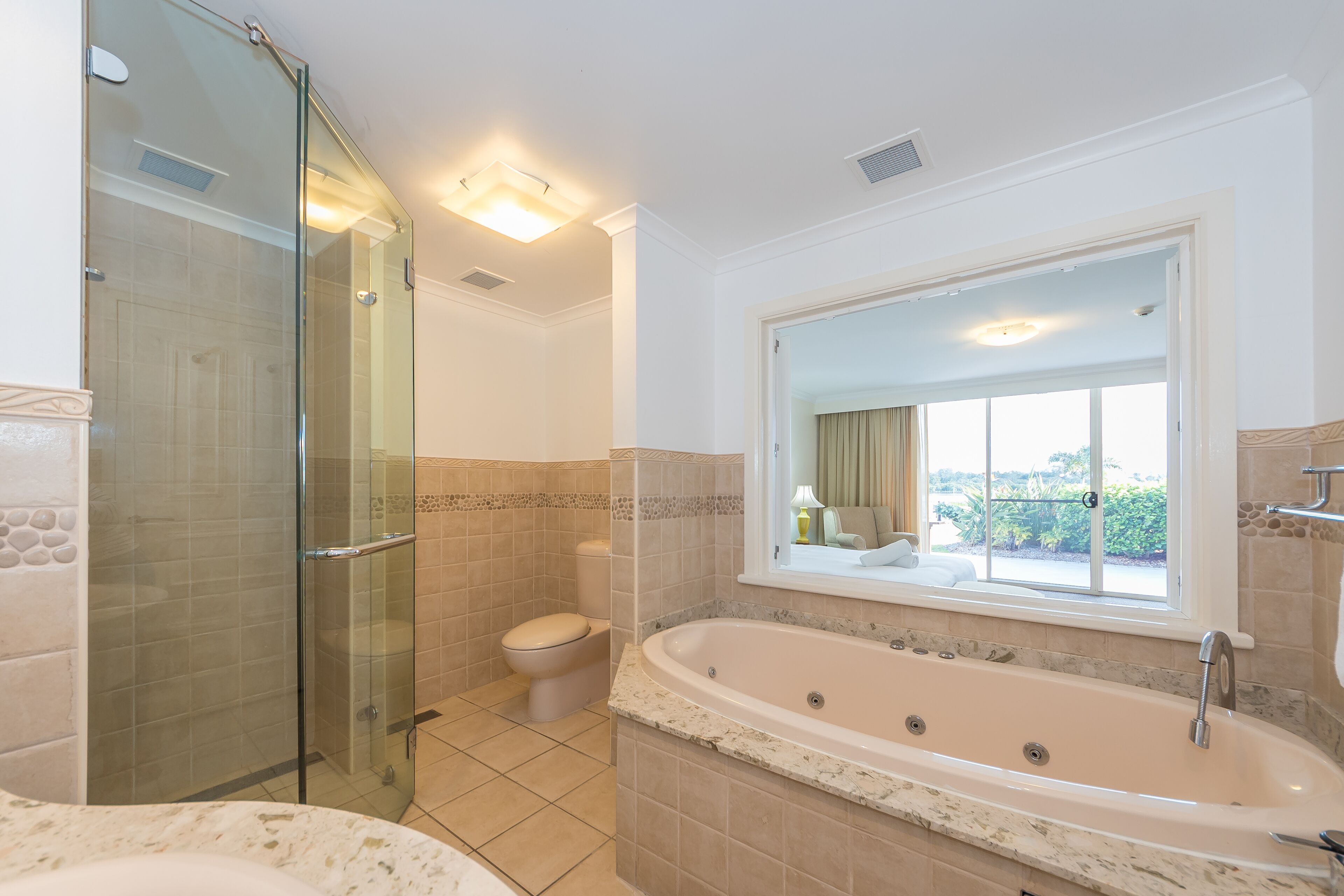 A bathroom with a glass shower enclosure, a toilet, a freestanding bathtub, and a window with a view of greenery.