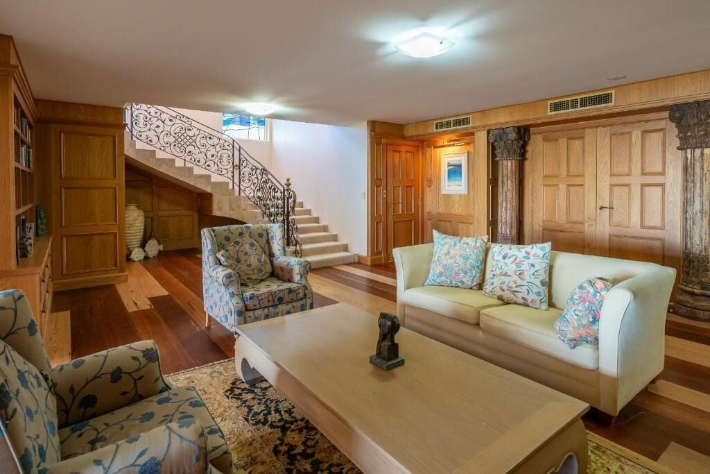 Una sala de estar con una escalera, un conjunto de sofá, una mesa de centro y paneles de madera.