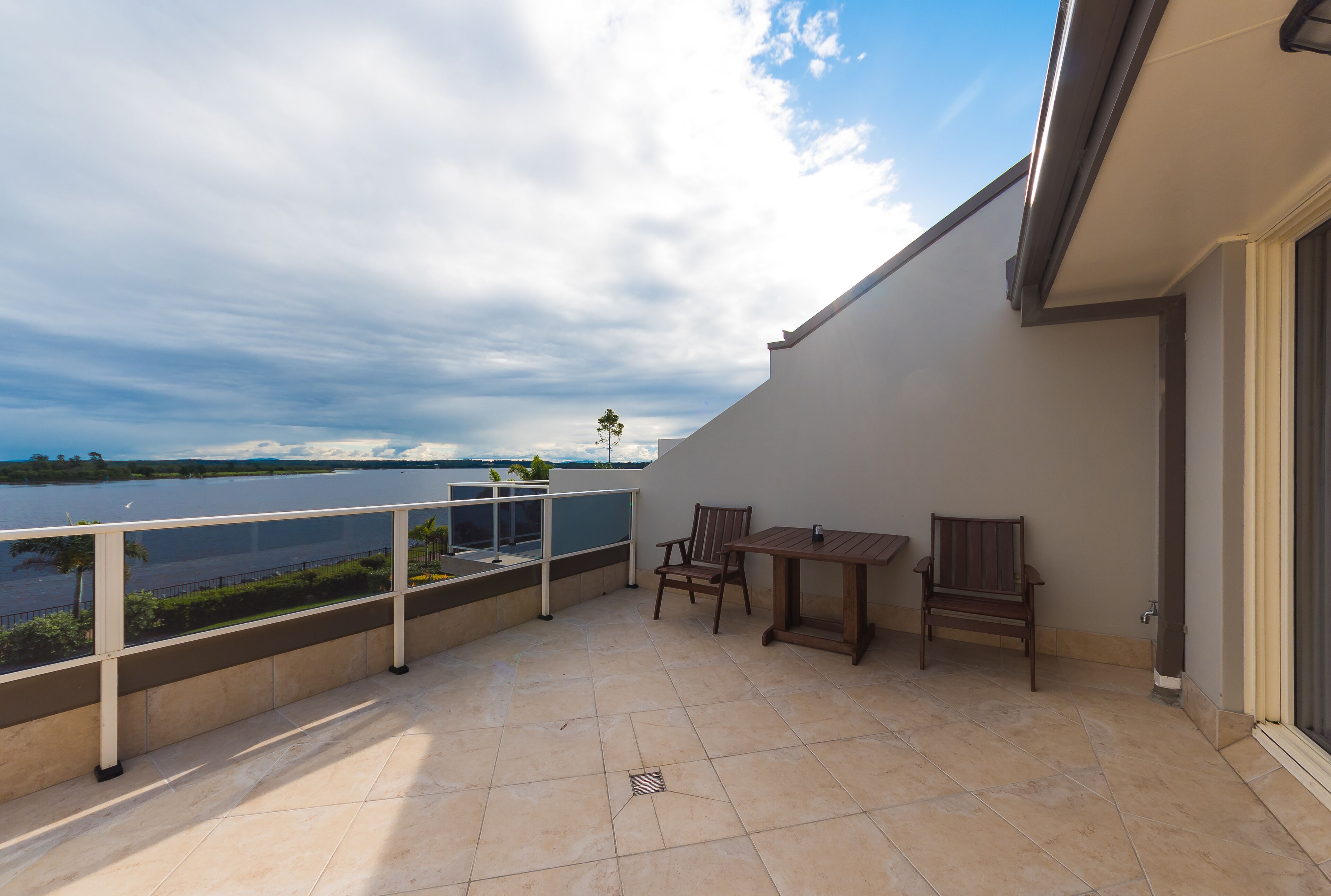 A balcony with a view of a lake, a table, and two chairs.
