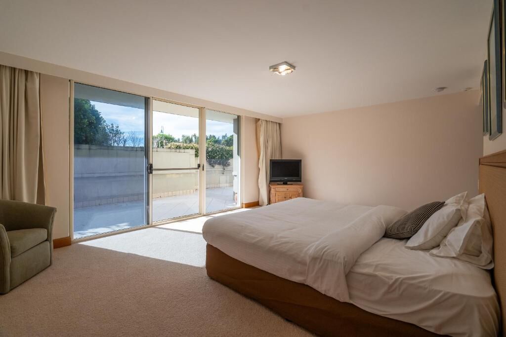 A bedroom with a large bed, a television on a wooden stand, and a sliding glass door leading to an outdoor area.