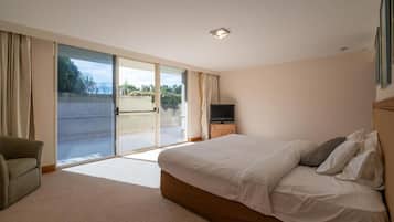 Ein Schlafzimmer mit einem großen Bett, einem Fernseher auf einem Holzboden und einer Glastür, die zu einem Außenbereich führt.