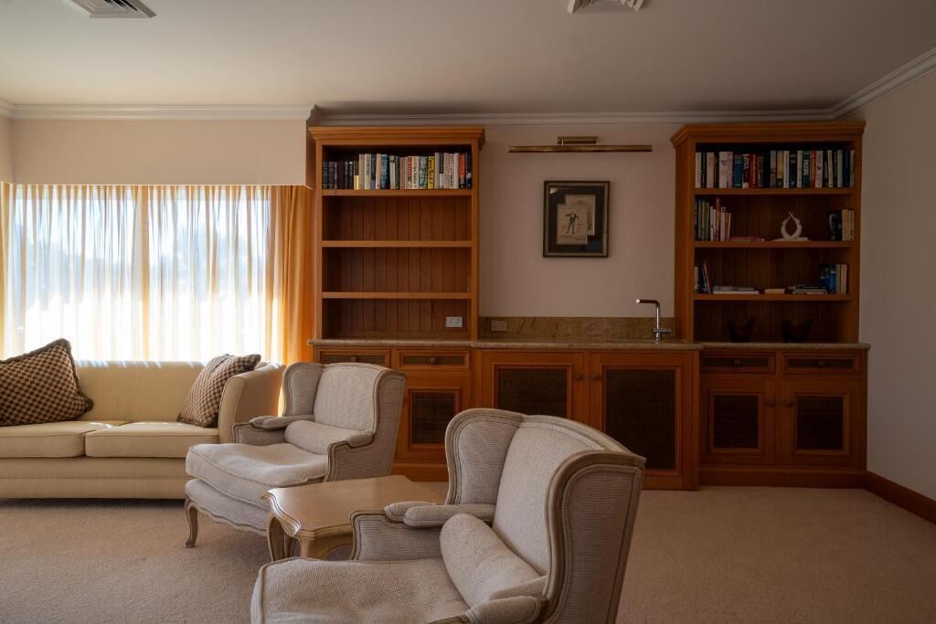 Un salon avec un canapé beige, deux fauteuils, une table basse et une bibliothèque remplie de livres.