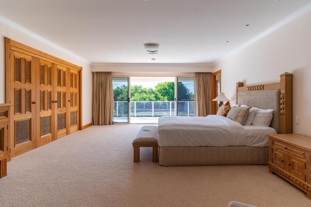 A bedroom with a large bed, a wooden wardrobe, and a balcony with curtains.