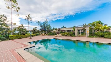 A swimming pool with a brick deck, lounge chairs, and a building in the background.
