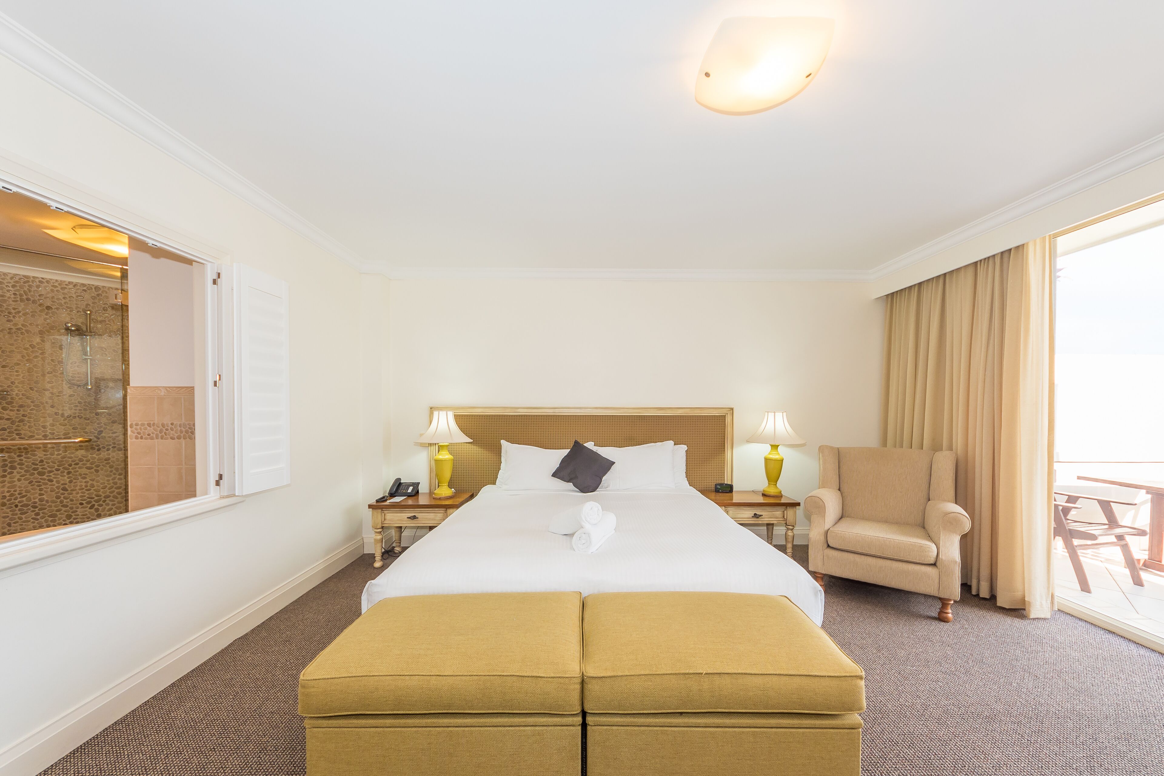 A hotel room with a large bed, a sitting area with a chair, a small table, and a view of the outside.