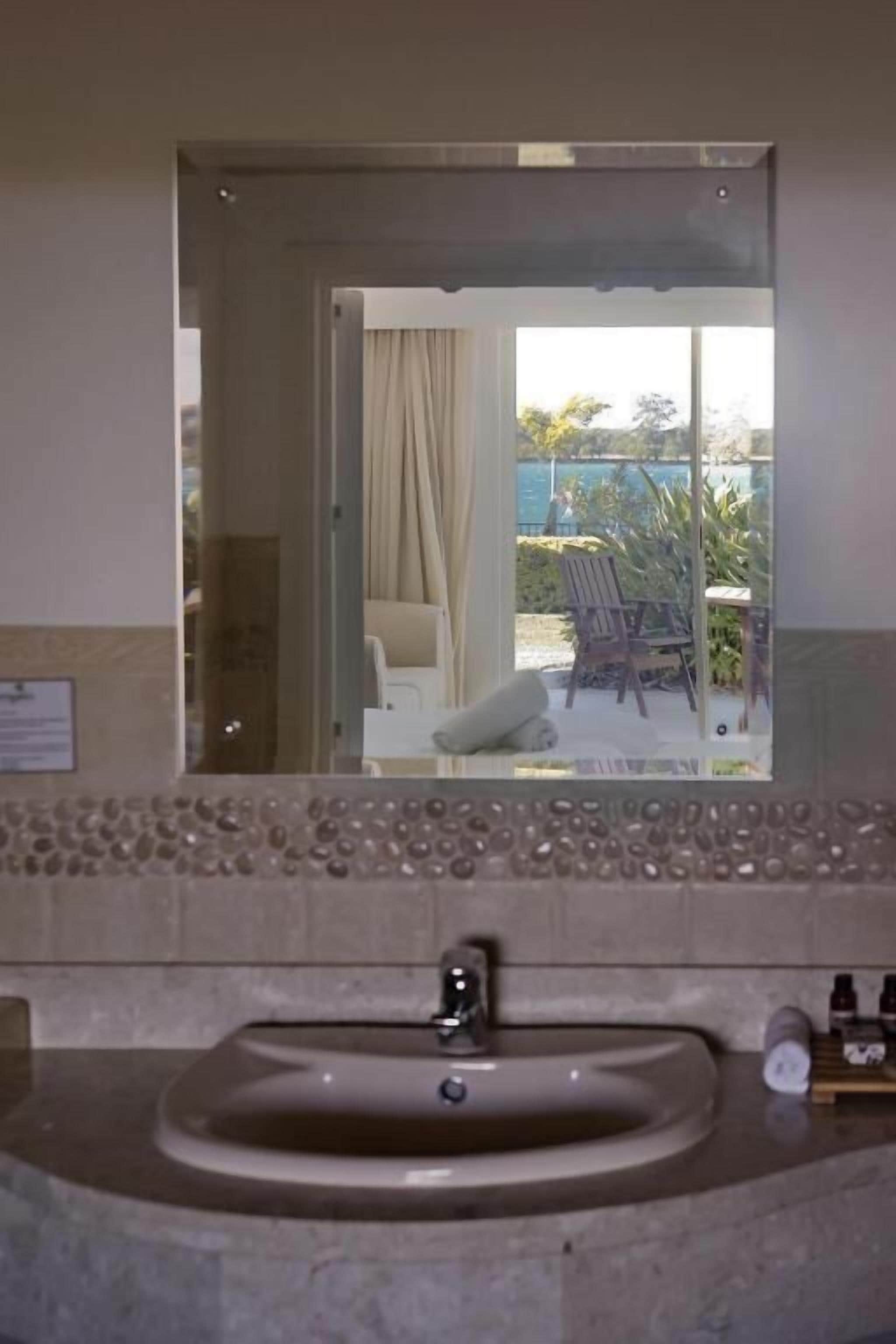 A bathroom with a sink, mirror, and a view of an outdoor area with a chair and plants.