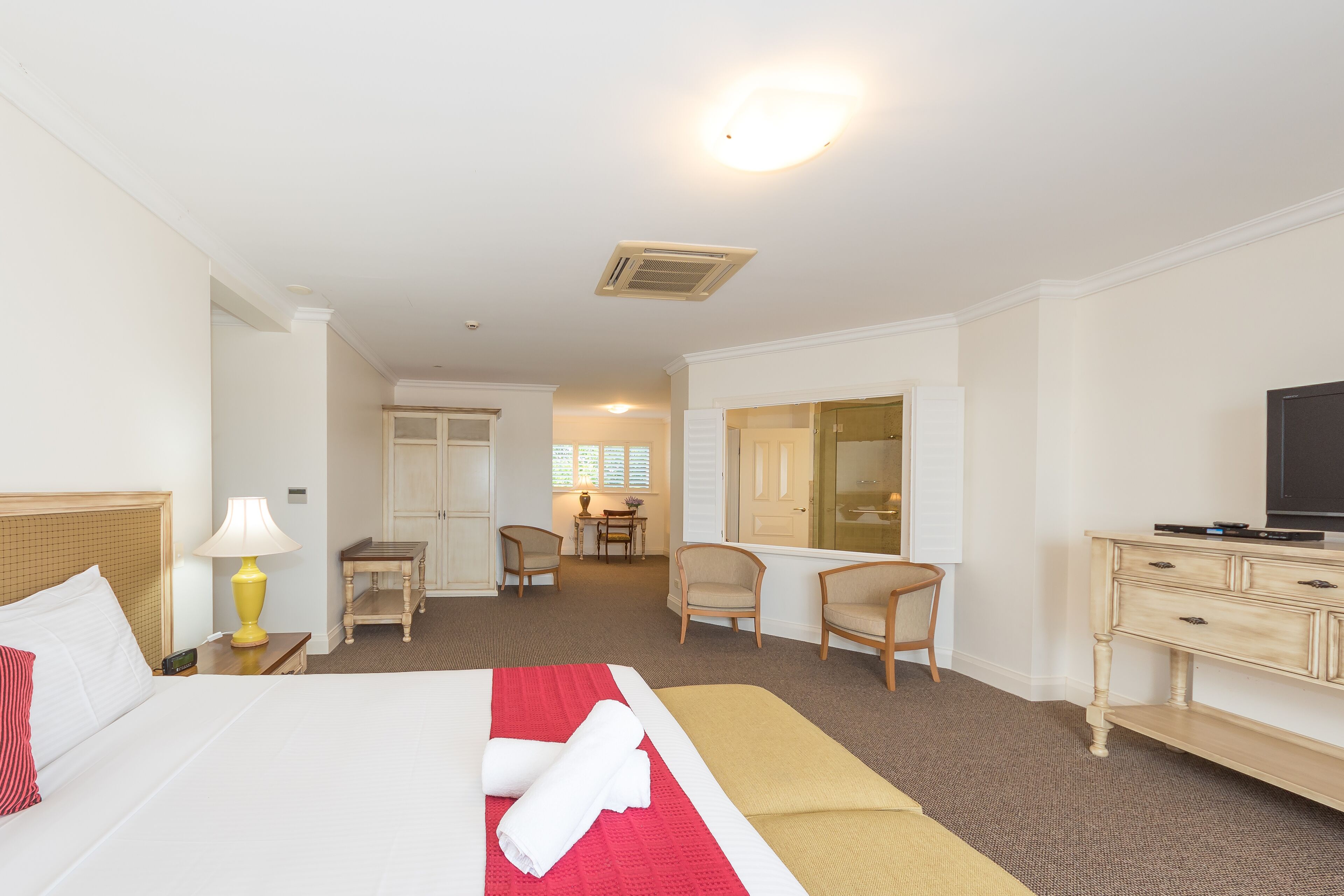 A hotel room with a bed, a desk, a chair, a television, and a bathroom visible through an open door.