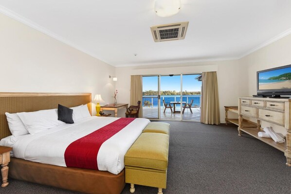 Habitación de hotel con cama, escritorio, televisión y vista al mar.
