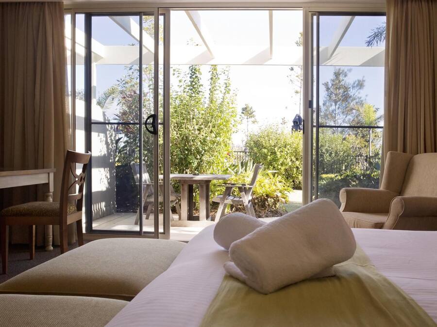 A hotel room with a bed, two chairs, a desk, and a balcony with a table and chairs.