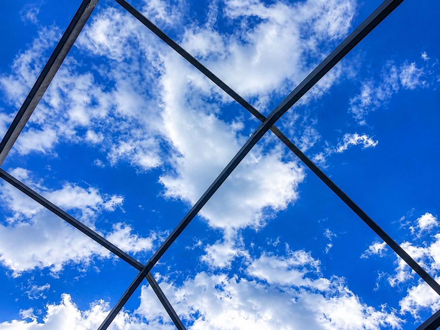 Ein klarer, blauer Himmel mit Wolken durch ein Metallgerüst.