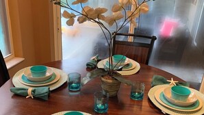 Et spisebord dækket med turkise og hvide tallerkener, skåle og servietter, med en plante som midtpunkt.