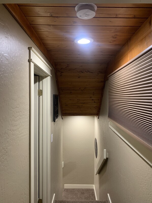 Un pasillo estrecho con vigas de madera en el techo, una puerta blanca y una ventana con persianas.
