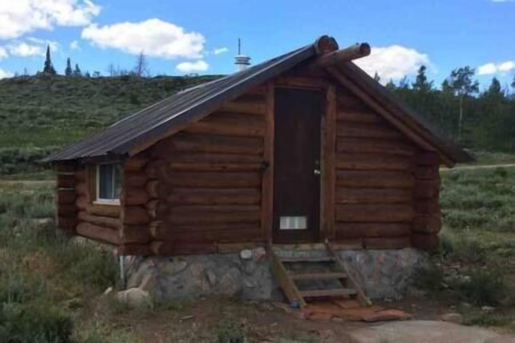 A small log cabin with a stone foundation, a single door, and a small porch.