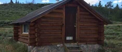 A small log cabin with a stone foundation, a single door, and a small porch.