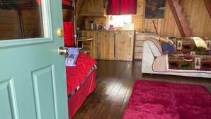 Una habitación con piso de madera, una cama con ropa de cama roja, un tapete rosa y un armario de madera con cortina roja.