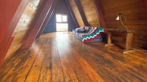Una habitación en el ático con suelos de madera, techo inclinado y una manta de colores en el suelo.