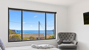 A bedroom with a large window offering a view of the ocean and a chair.