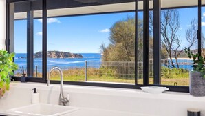 A bathroom with a large window offering a view of the sea and hills.