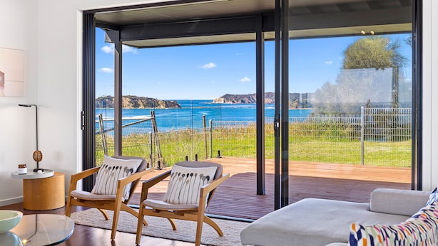 A modern living room with a large sliding glass door leading to a deck with a view of the sea.