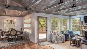 A spacious living area with a high ceiling, a dining area with a chandelier, and large windows with blinds.