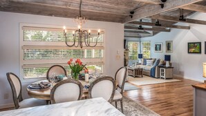 A dining area with a wooden ceiling, large windows with blinds, and a chandelier.