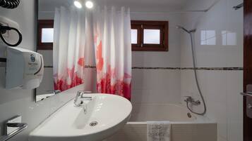 Un baño con lavamanos blanco, espejo, ducha y ventana con marco de madera.