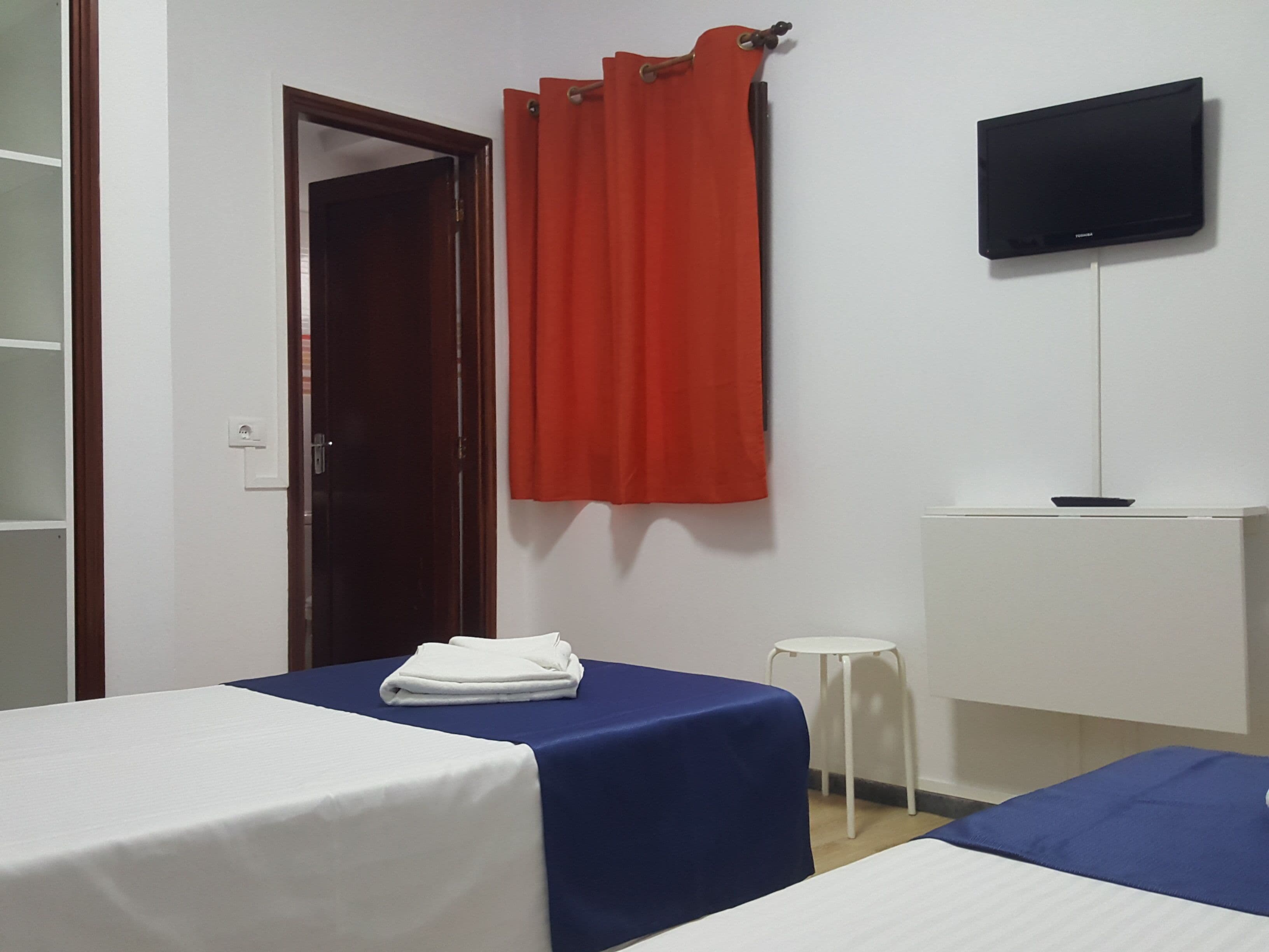 Een hotelkamer met twee bedden, een televisie, een bureau en een rood gordijn.