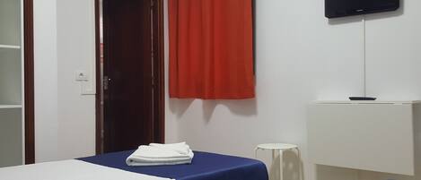 Een hotelkamer met twee bedden, een televisie, een bureau en een rood gordijn.