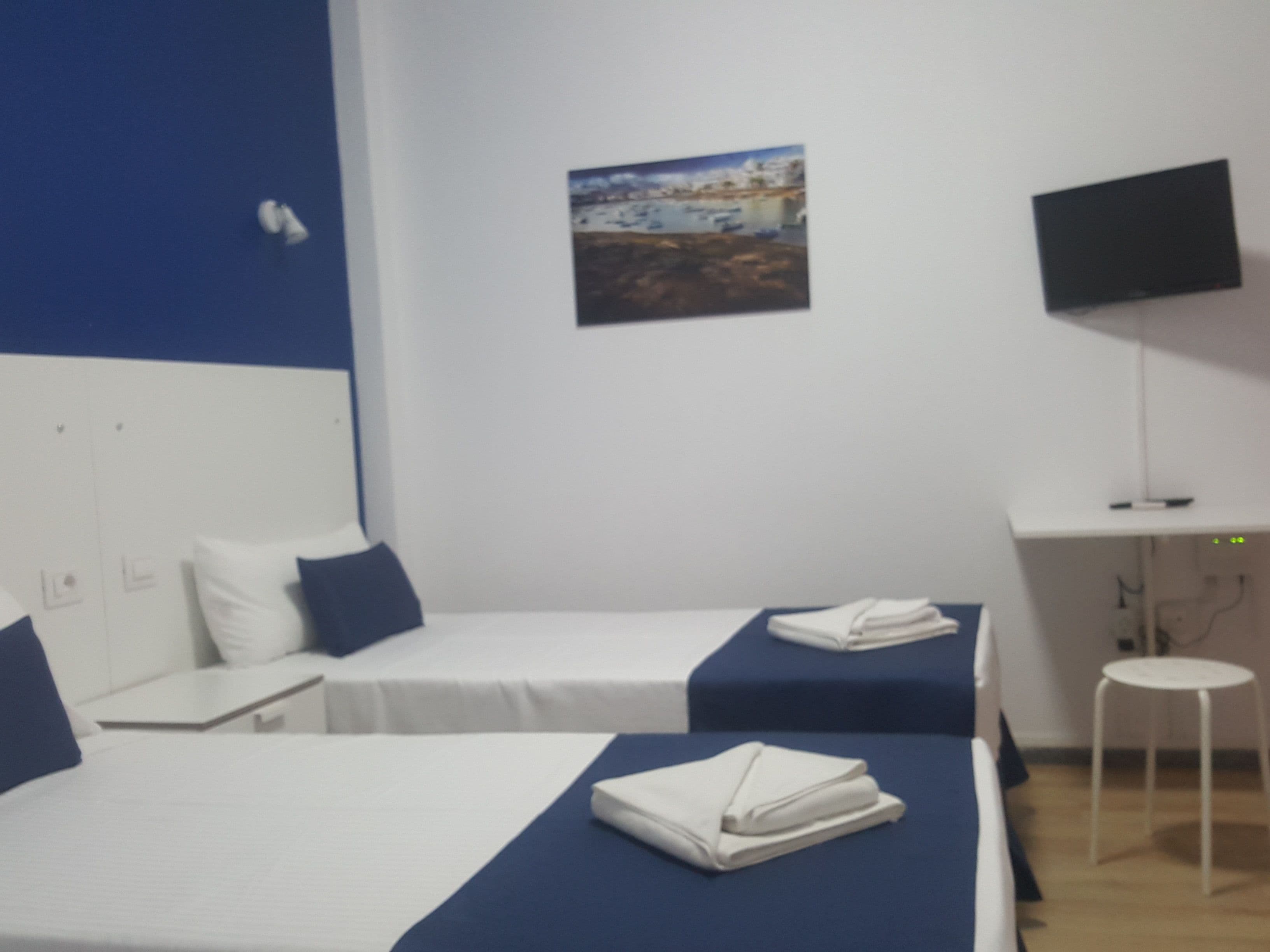 Une chambre d’hôtel avec deux lits, un bureau, une chaise, un téléviseur à écran plat et un tableau accroché au mur.