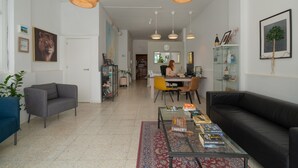 Una sala de estar moderna con una mesa de centro de vidrio, un sofá negro y una zona de comedor con una silla amarilla.