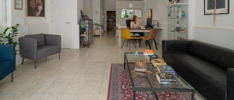 Een moderne woonkamer met een glazen salontafel, een zwarte bank en een eethoek met een gele stoel.