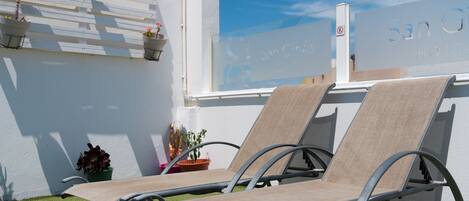 Two lounge chairs with metal frames and beige fabric, positioned on artificial grass, against a white wall with a window.